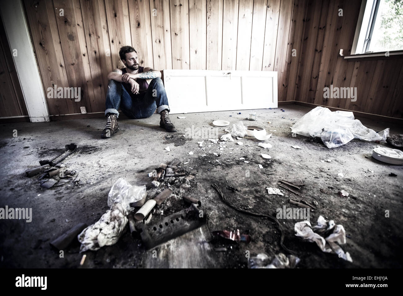 Mann oder Redneck sitzt auf dem Boden und Rauch in einem unordentlichen Haus. Stockfoto