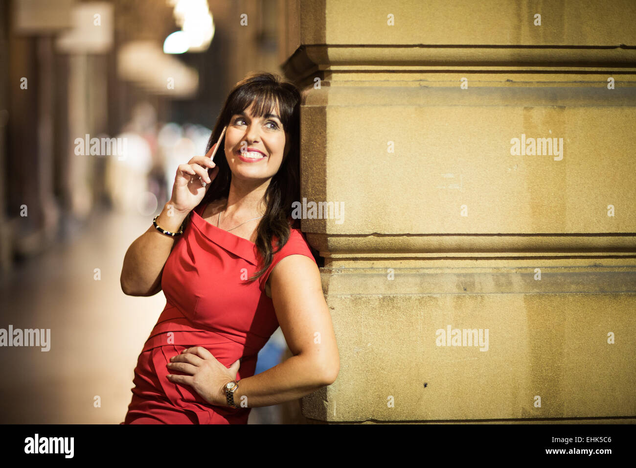Eine glückliche lächelnde Frau in ihrem 40 ist auf ihrem mobilen Gerät im alten Teil der Stadt sprechen. Stockfoto