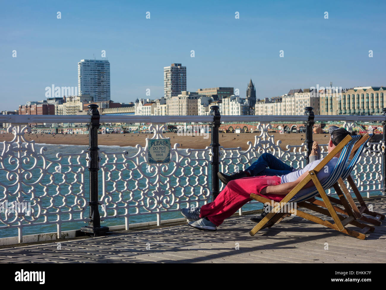 Touristen sitzen auf Liegestühlen am Pier von Brighton Stockfoto