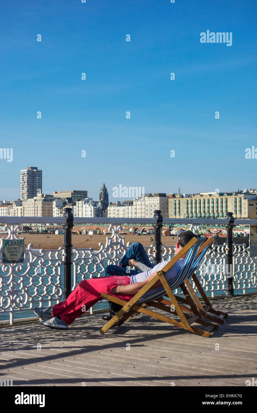 Touristen sitzen auf Liegestühlen am Pier von Brighton Stockfoto