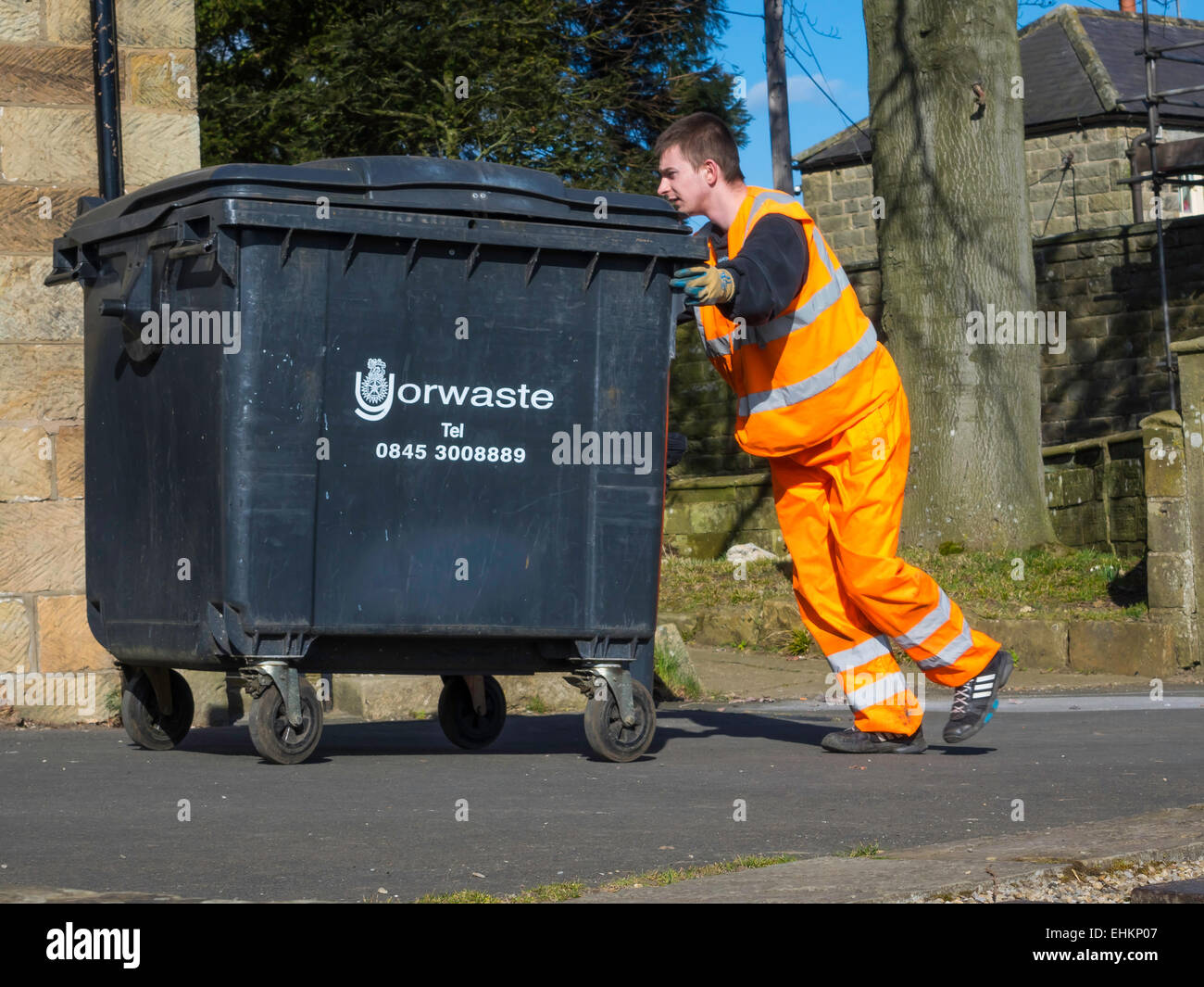 Ein Abfall Entsorgung Operative in Warnkleidung zurückschieben eine kommerzielle Größe Wheelie bin in ein Café nach Trinkgeld. Stockfoto