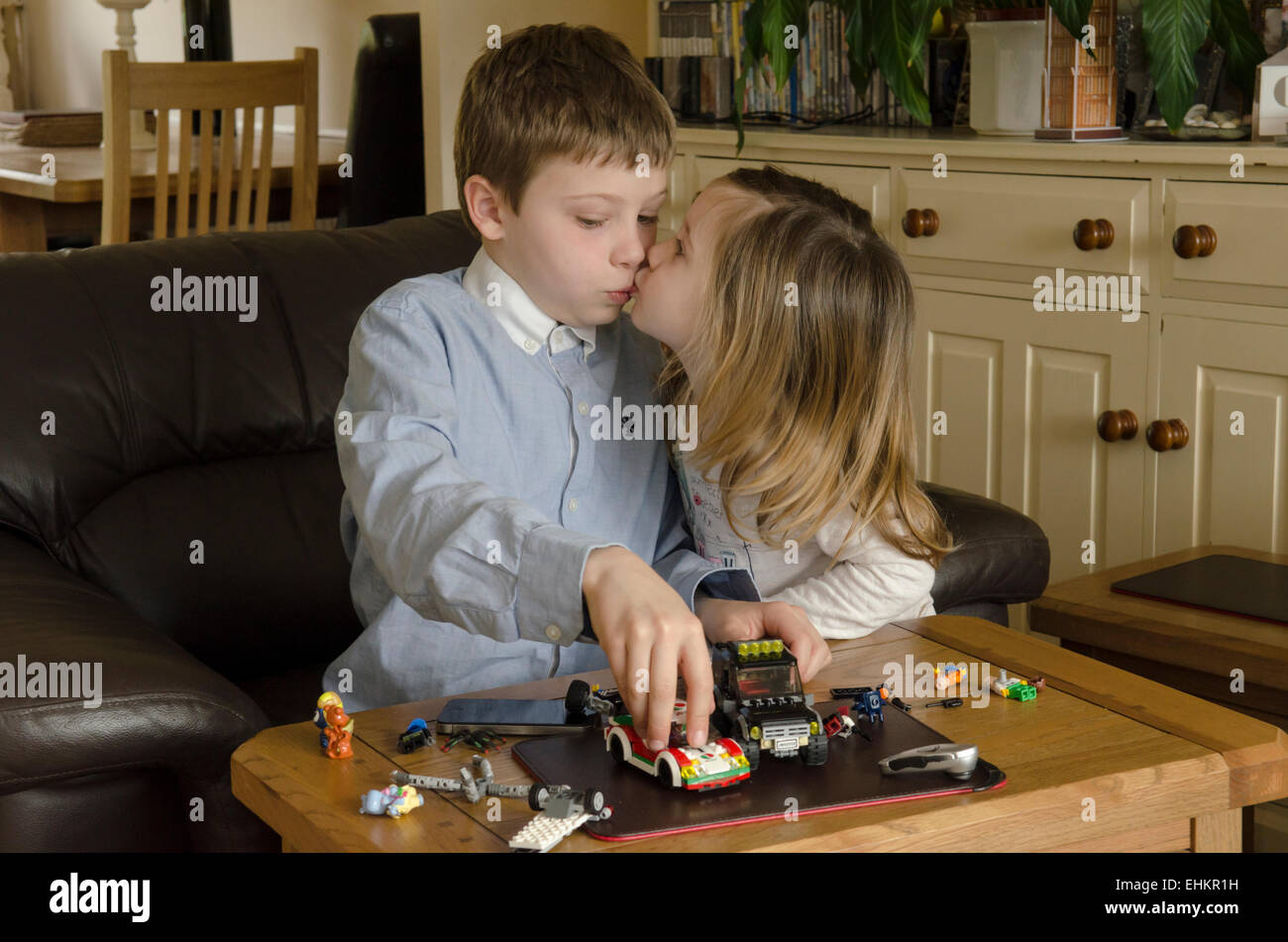 Junge, acht Jahre alt, mit Schwester, spielen zwei Jahre alt, mit Lego zusammen. Mädchen küssen Junge, aber er spielt beschäftigt, UK. Stockfoto