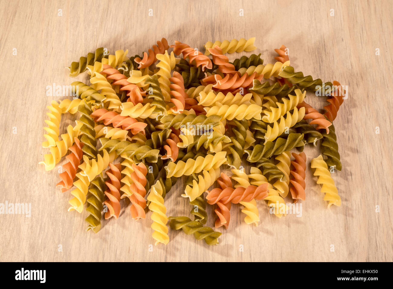 Ein kleines Häufchen von drei verschiedenen Farben von Fusilli auf einem Holztisch. Stockfoto