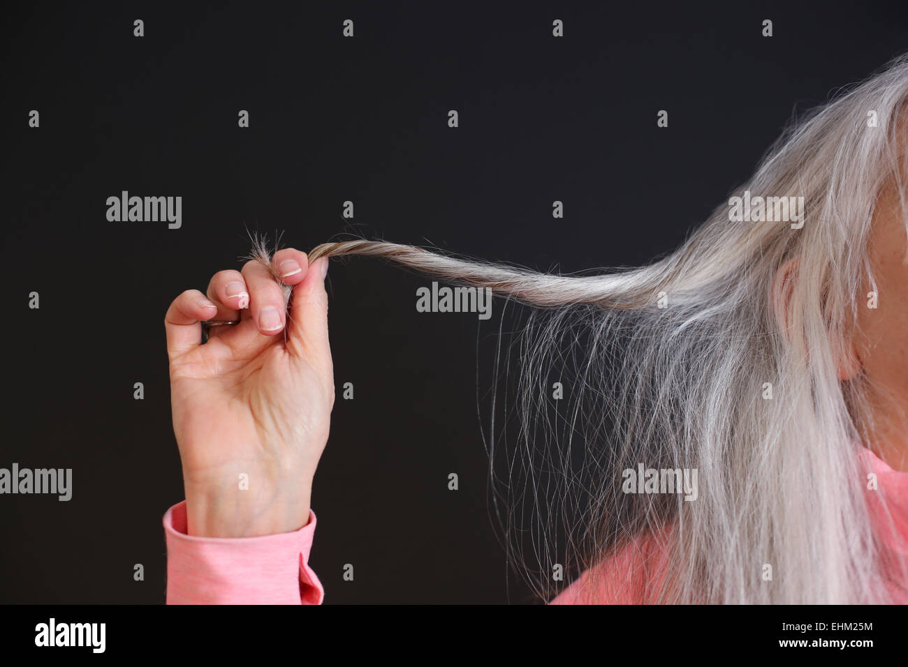 Eine hochrangige Frau hält einen Strang der grauen Haare. Stockfoto