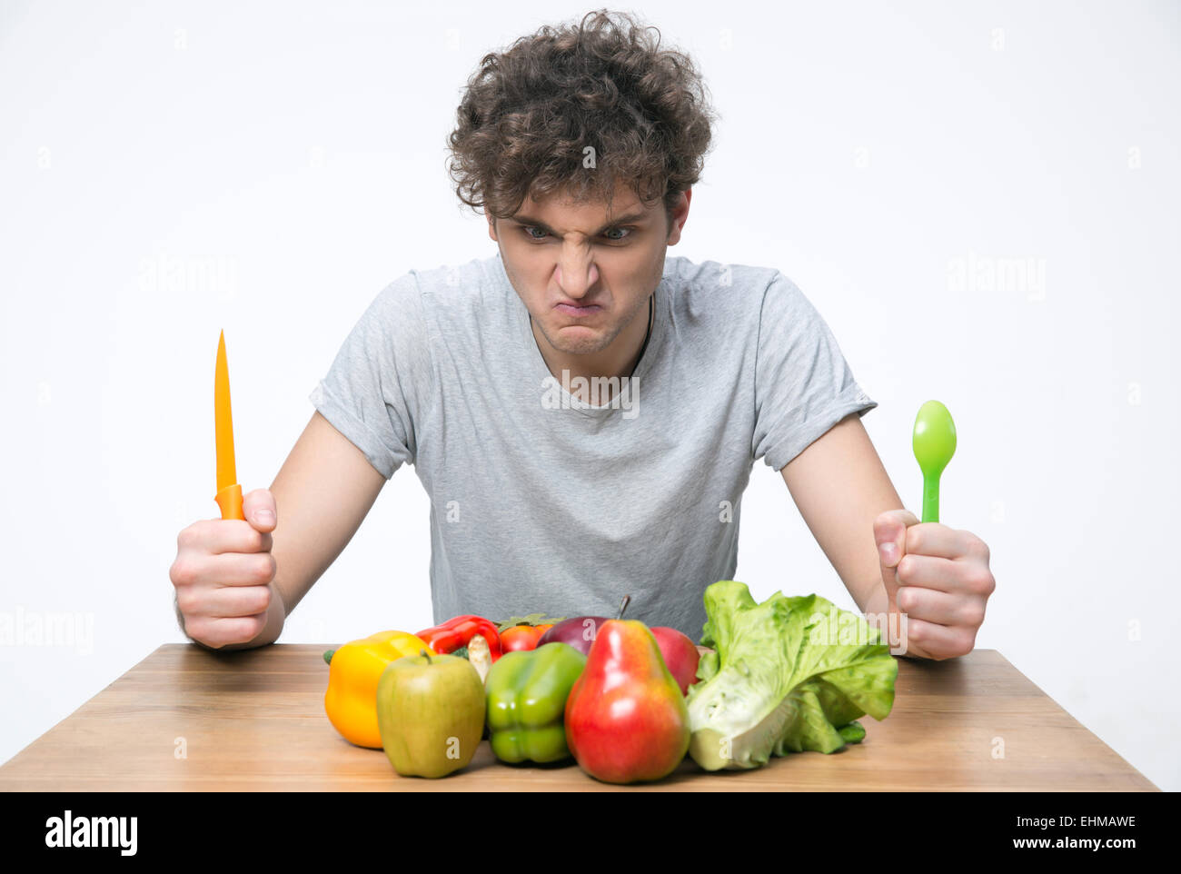 Verärgerter Mann sitzt am Tisch mit Gemüse Stockfoto