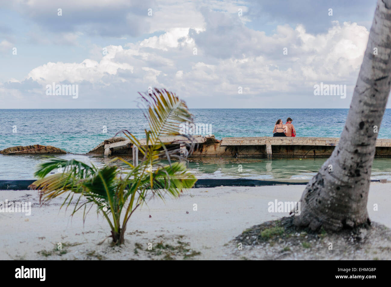 Ein paar sitzen zusammen auf der alten Mole am öffentlichen Strand auf Caye Caulker, Belize Stockfoto
