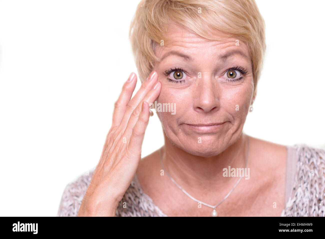 Attraktive senior blonde Frau mit einem weit aufgerissenen Augen Ausdruck und ihre Brille auf dem Kopf überprüfen ihr Teint Stockfoto
