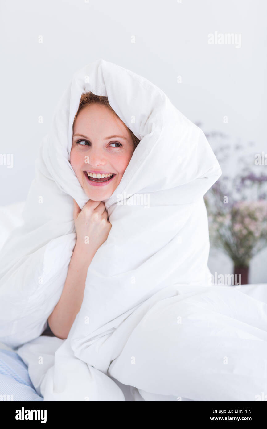 Verspielte Frau eingewickelt in Bettdecke über Kopf auf Bett Stockfoto