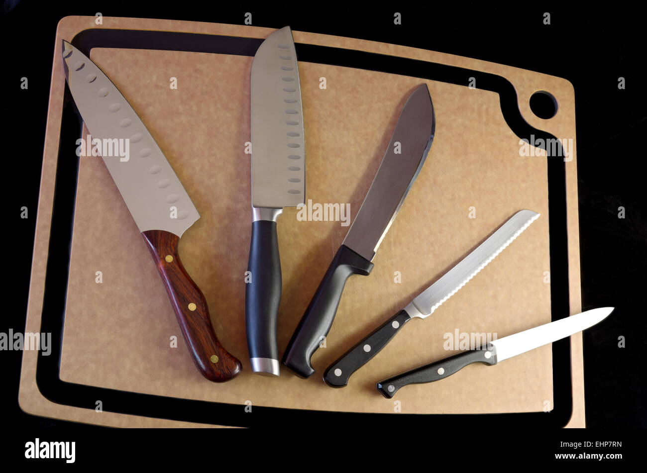 Fünf Messer aus Edelstahl auf Schneidebrett auf schwarzem Hintergrund Stockfoto