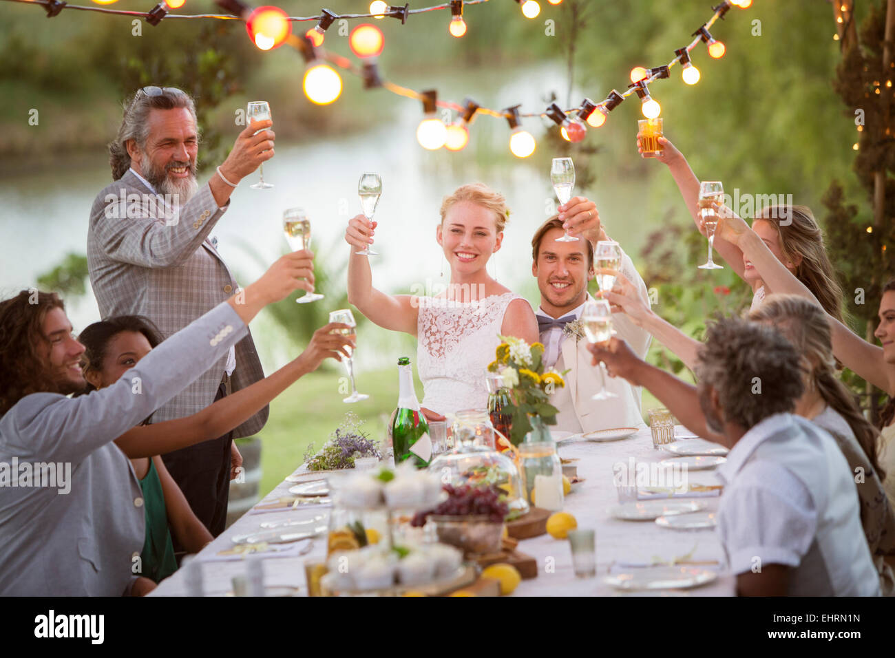 Junges Paar und ihre Gäste während der Hochzeitsfeier im Garten mit Champagner Toasten Stockfoto