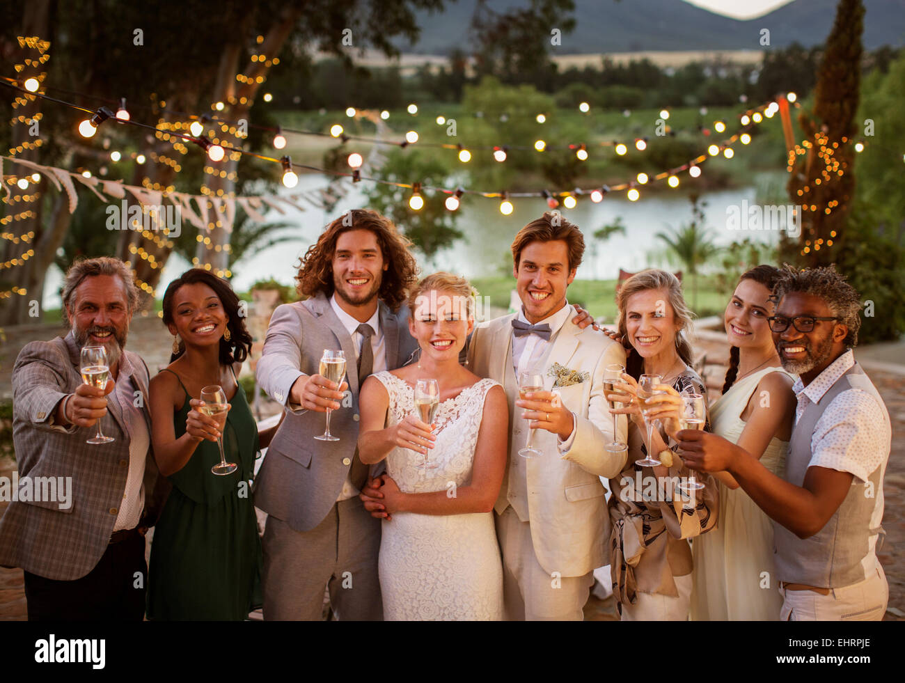 Porträt eines jungen Paares mit Gästen Toasten mit Champagner während der Hochzeitsfeier in der Abenddämmerung Stockfoto