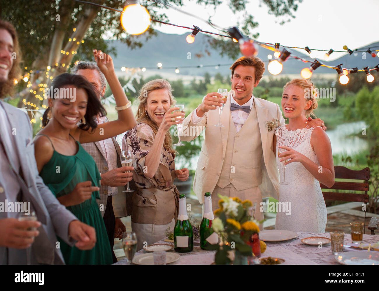 Junge Paare und Gäste Toasten mit Champagner während der Hochzeitsfeier im heimischen Garten Stockfoto