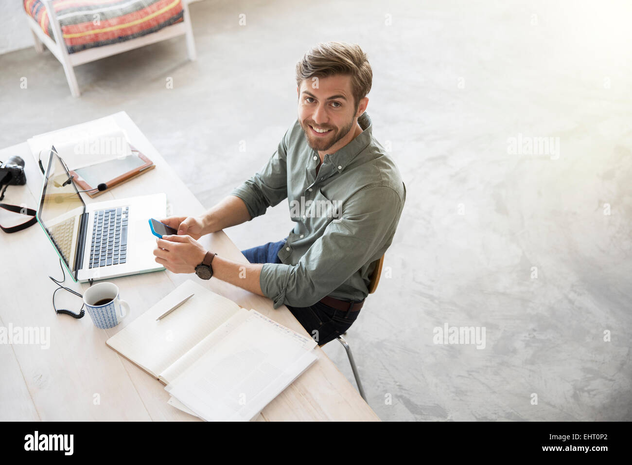 Porträt von junger Mann mit Handy und Laptop am Schreibtisch sitzen Stockfoto