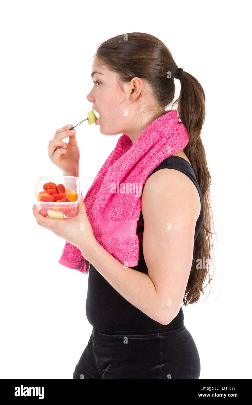 Junge Frau in Sportkleidung mit Handtuch Essen frisches Obst, isoliert auf weißem Hintergrund Stockfoto