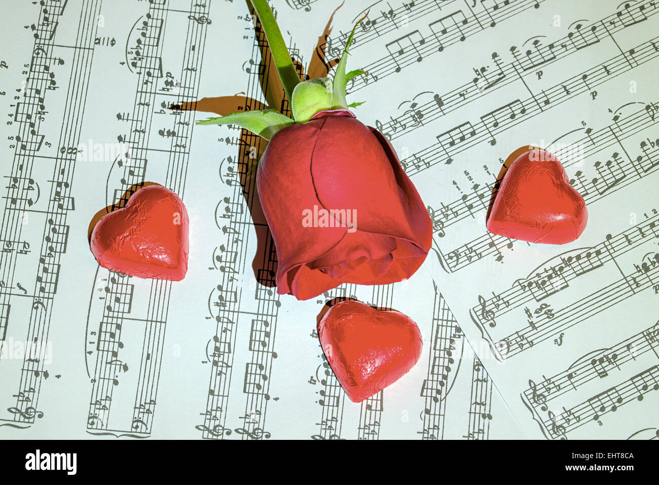 Rote Rose auf Partituren mit Schokoladenherzen rund um Stockfoto