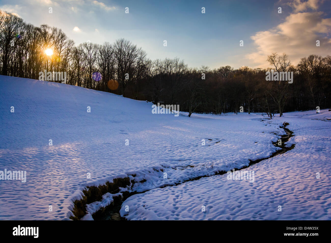 Sonnenuntergang über einem Bach in einem schneebedeckten Feld in ländlichen Baltimore County, Maryland. Stockfoto