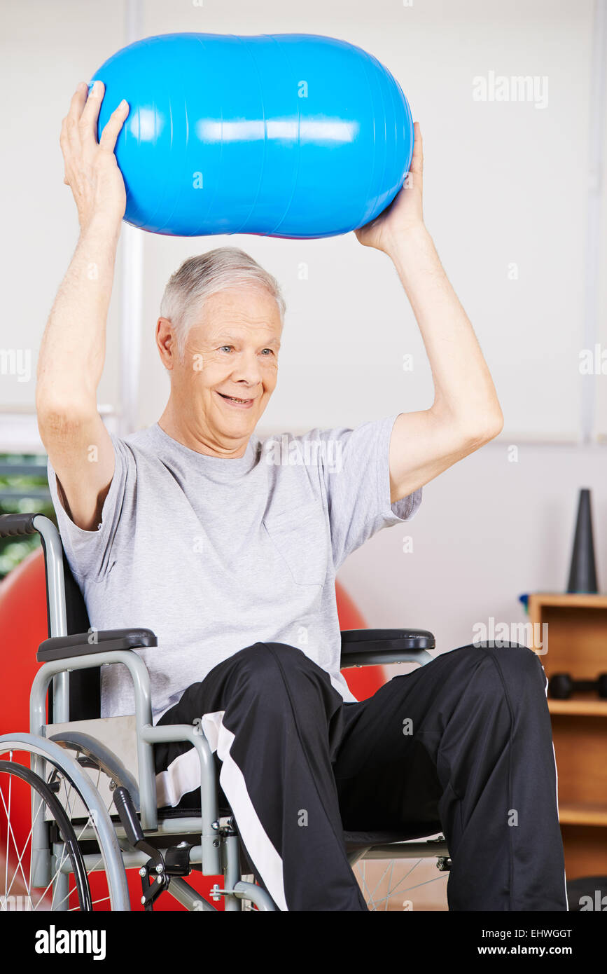 Alter Mann im Rollstuhl in der Psychotherapie heben einen Gymnastikball Stockfoto