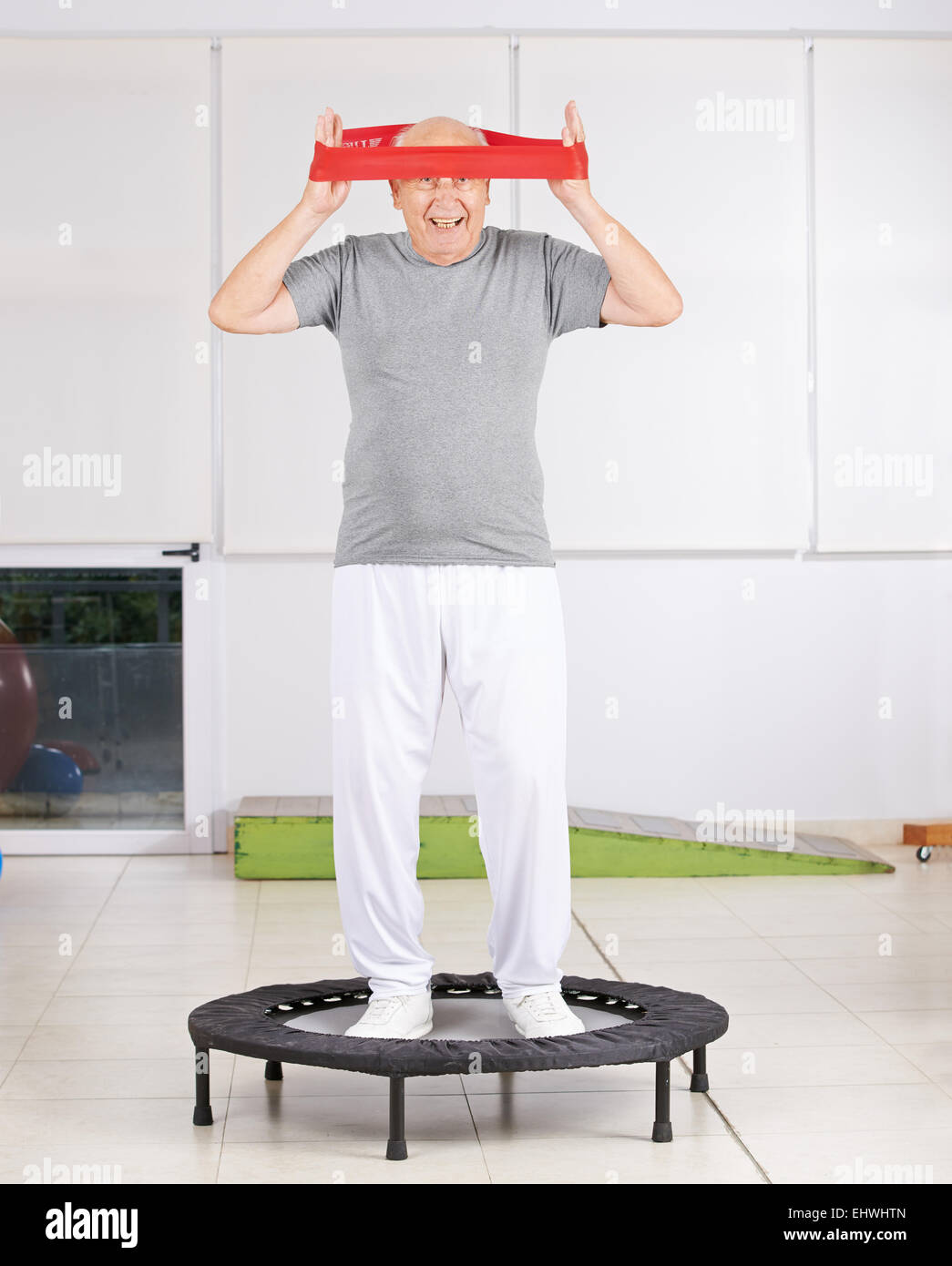 Alter Mann Spaß mit Übungsband in der Physiotherapie auf einem Trampolin Stockfoto