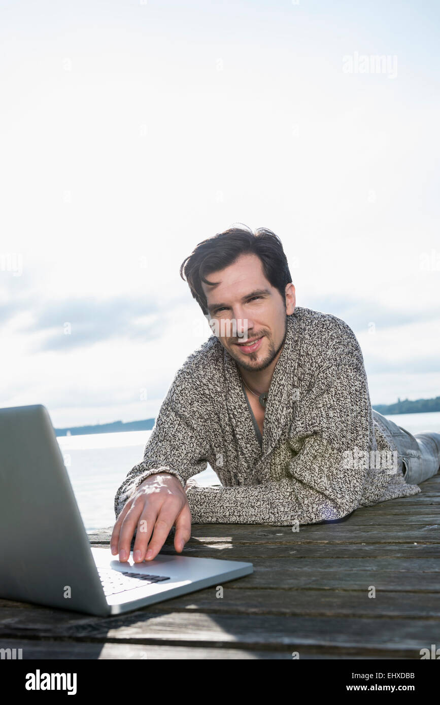 Portrait Mann liegend auf Holzsteg mit laptop Stockfoto