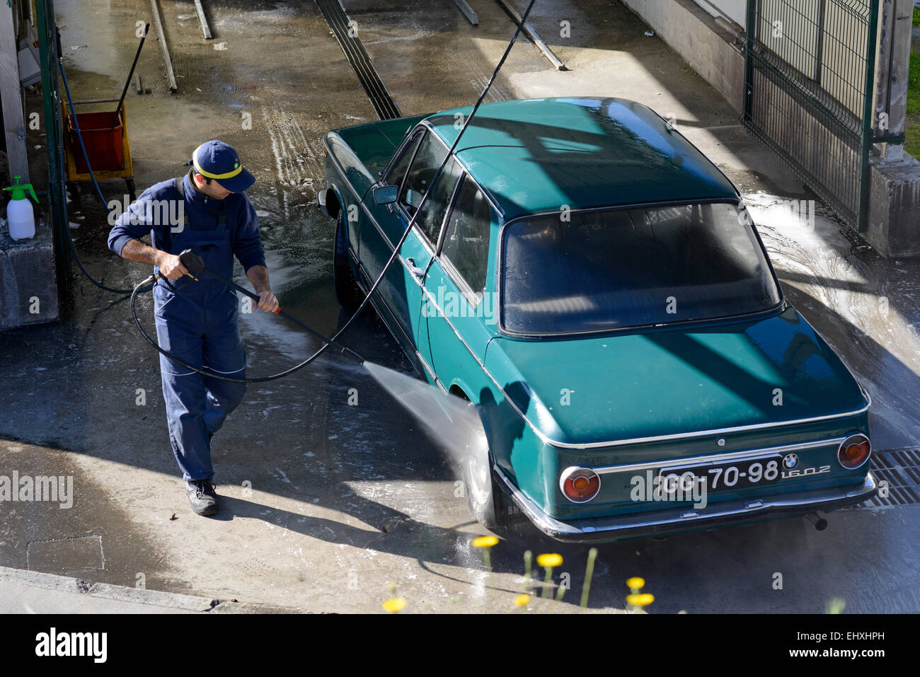 Junger Mann Waschen Auto mit Hochdruck-Wasserschlauch an eine professionelle Fahrzeugreinigung Stockfoto