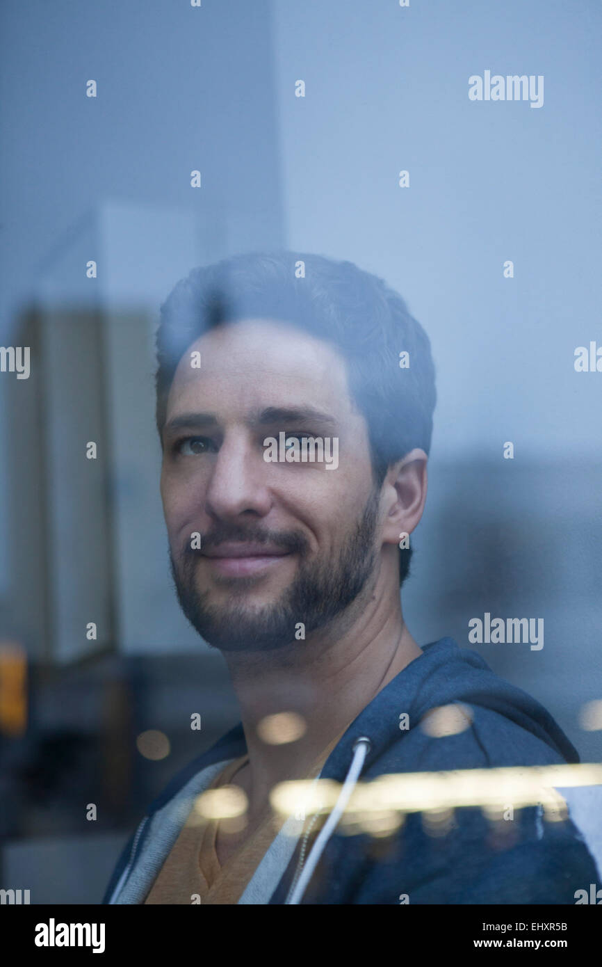 Porträt von lächelnden Mann mit Bart Blick durch Fenster Stockfoto