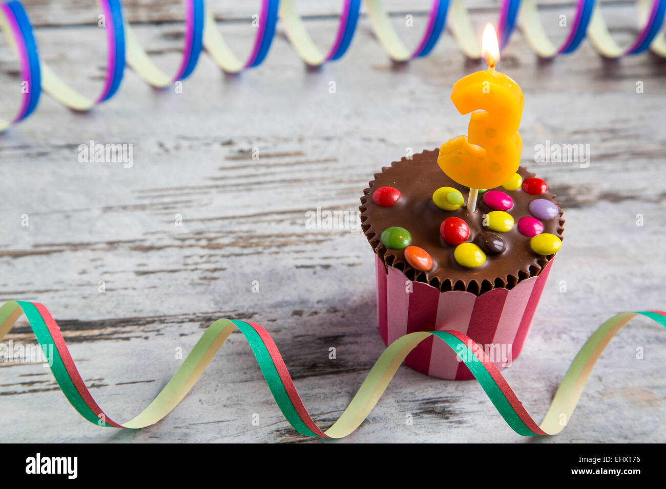 GeburtstagMuffins mit Schokolinsen und brennende Kerze Stockfotografie