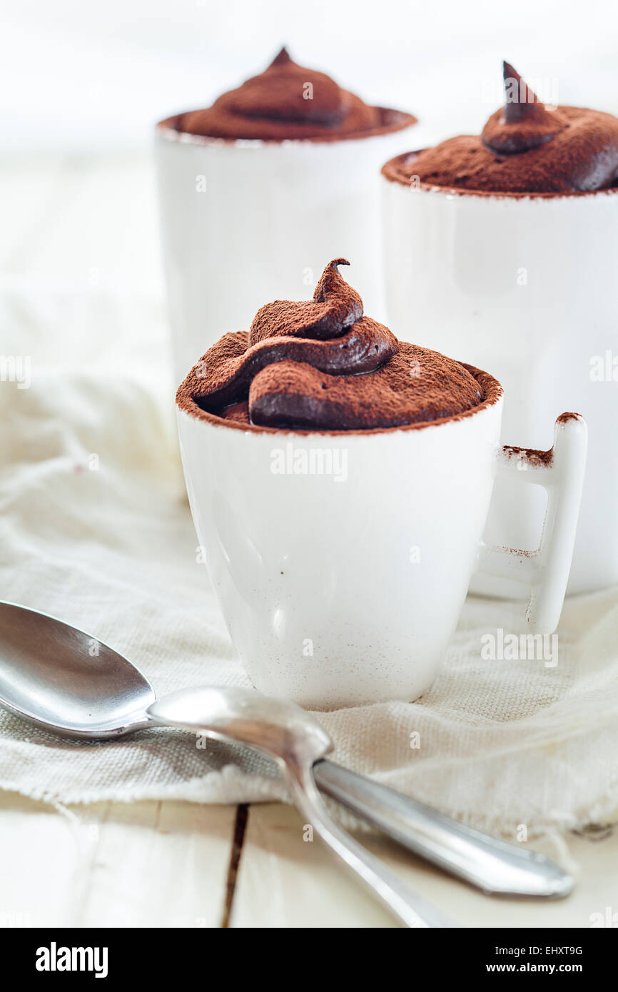 Drei Tassen vegane Mousse au Chocolat, Teelöffel, Tuch auf weißem Holz Stockfoto