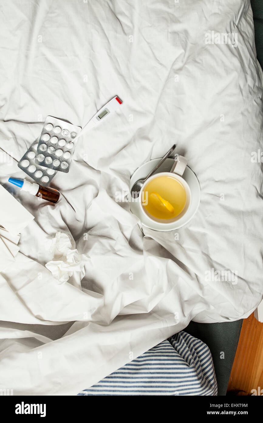 Zitrone-Infusion, Thermometer, Tabletten, Nasenspray und Gewebe im Bett Stockfoto