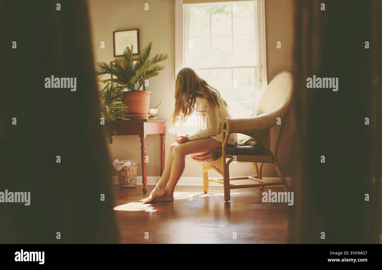 Junge Frau sitzt auf einem Stuhl im Wohnzimmer Stockfoto