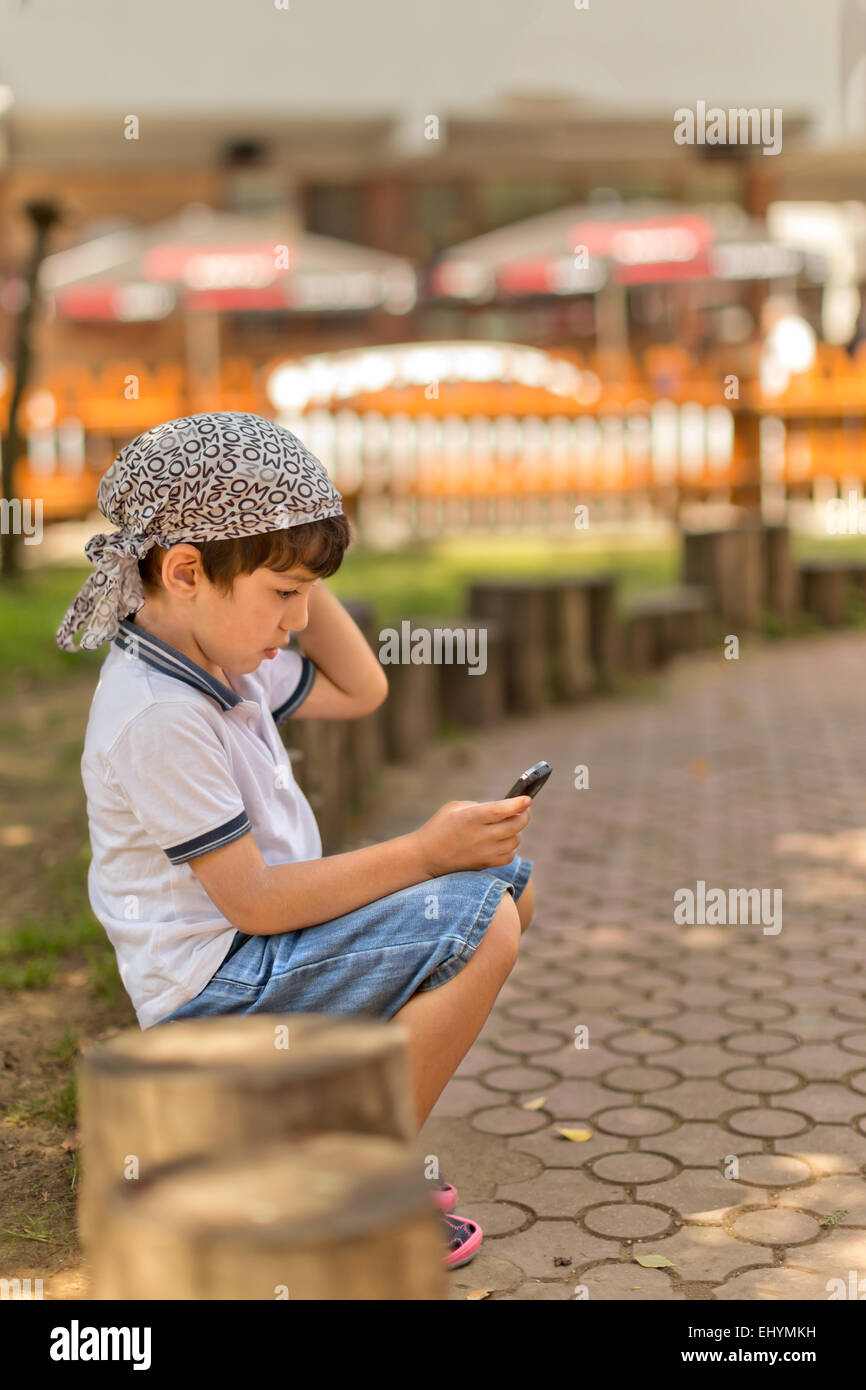 Junge sitzt im Park Blick auf Handy Stockfoto