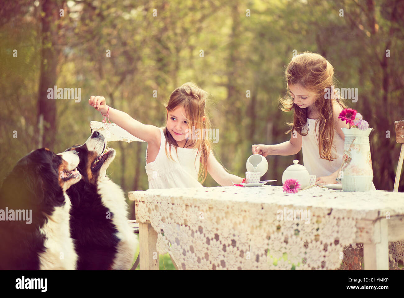Zwei Mädchen, die eine Tee-Party im Garten mit zwei Hunden Stockfoto