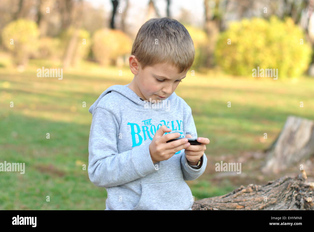 Junge spielt auf mobilen Gerät im park Stockfoto