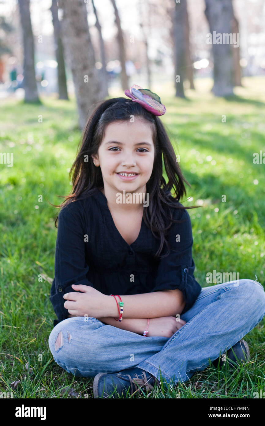 Lächelndes Mädchen sitzt mit gekreuzten Beinen im park Stockfoto