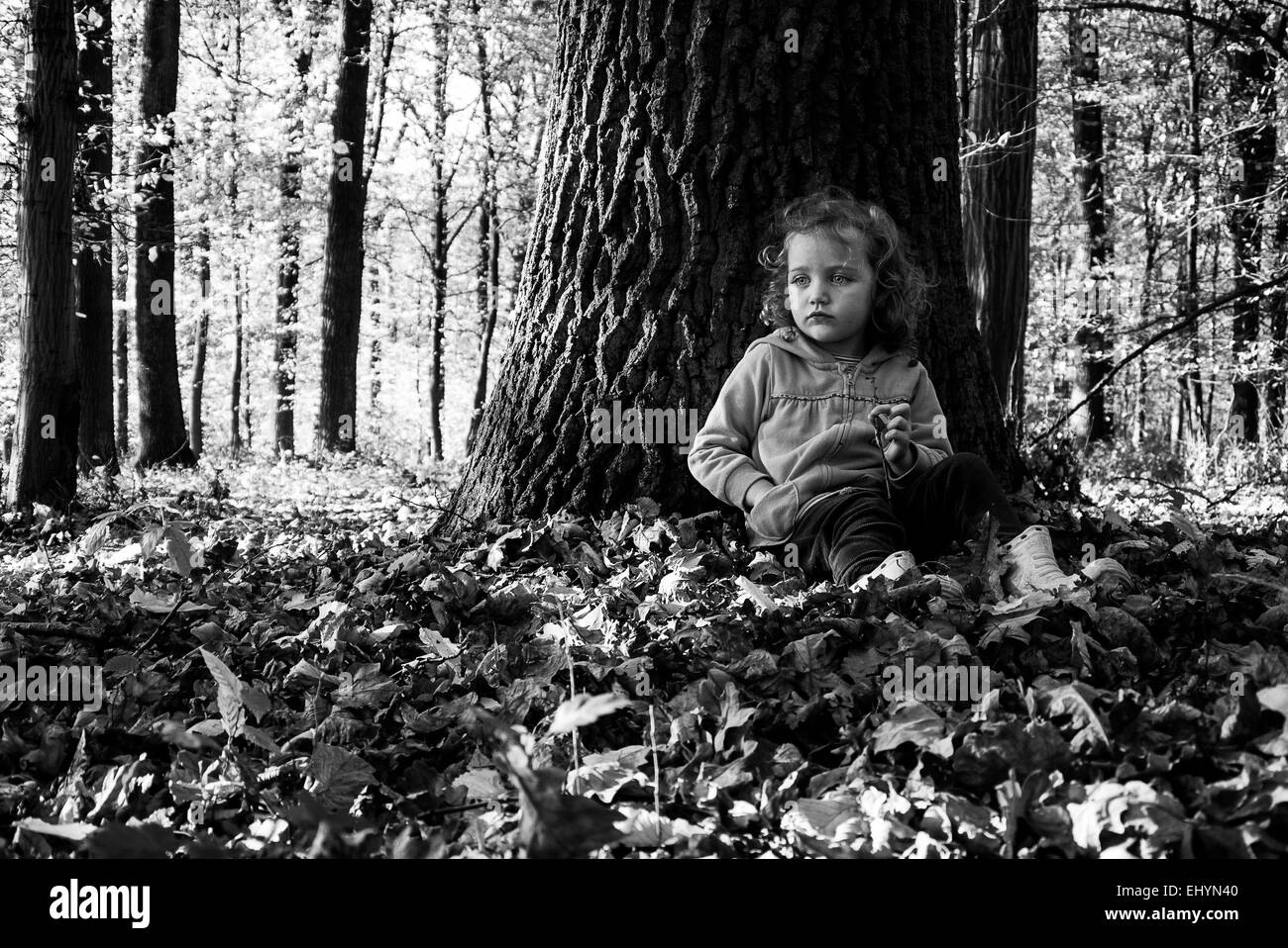 Mädchen, das im Wald sitzt und sich an einen Baumstamm lehnt, Polen Stockfoto