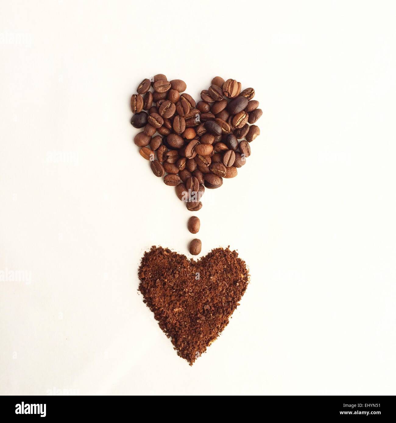 Kaffeebohnen in Form eines Herzens, tropft in ein anderes Herz Form des gemahlenen Kaffees Stockfoto