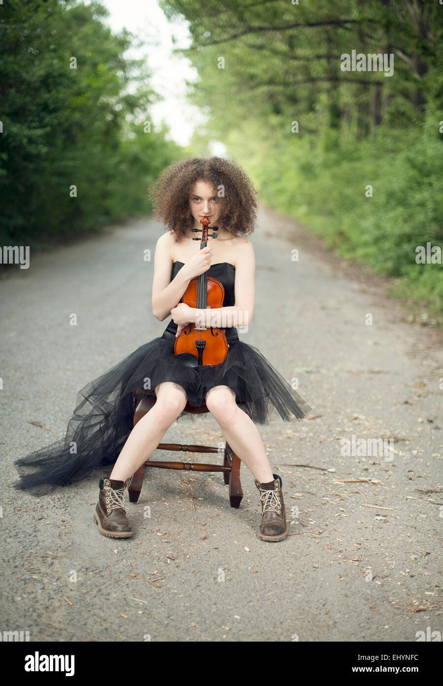 Junge Frau in einem schwarzen Kleid sitzt mit ihrer Violine Stockfoto