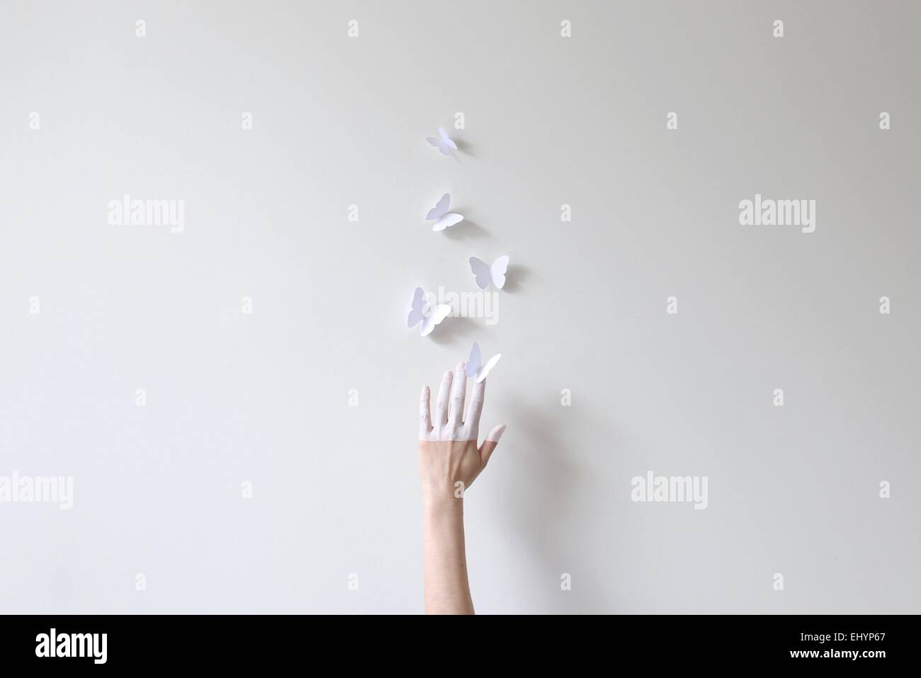 Eine Hand, die Hälfte in weißen Griff nach Papier Schmetterlinge gegen die weiße Wand gemalt Stockfoto