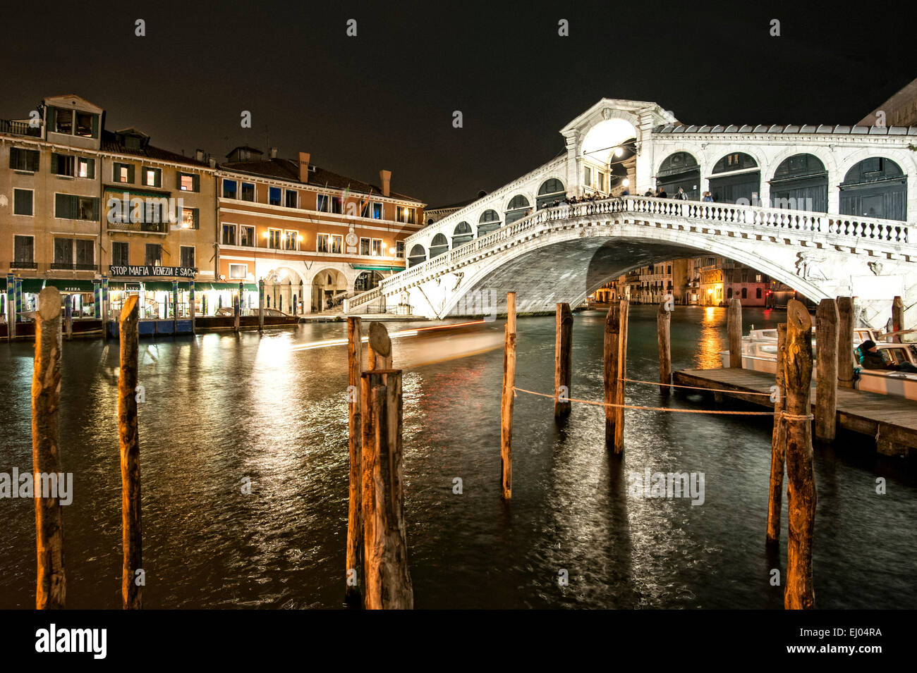 Pier mit Boot am Canal Grande bei der Rialto-Brücke in der Nacht. Stockfoto
