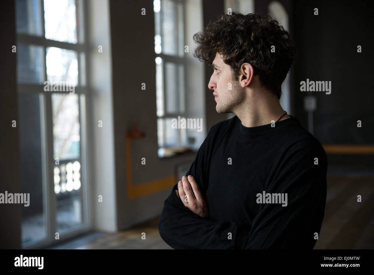 Hübscher junger Mann mit lockigem Haar stehend mit Armen gefaltet in Turnhalle Stockfoto