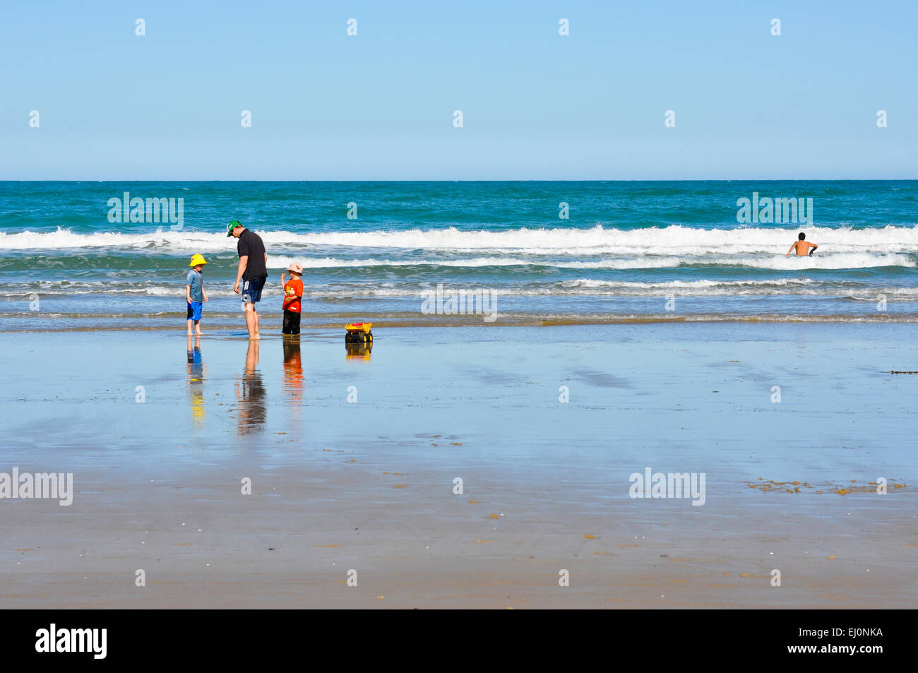 Familie spielen auf australischen Strand mit Schwimmer in der Brandung auf der rechten Seite des Bildes. Stockfoto