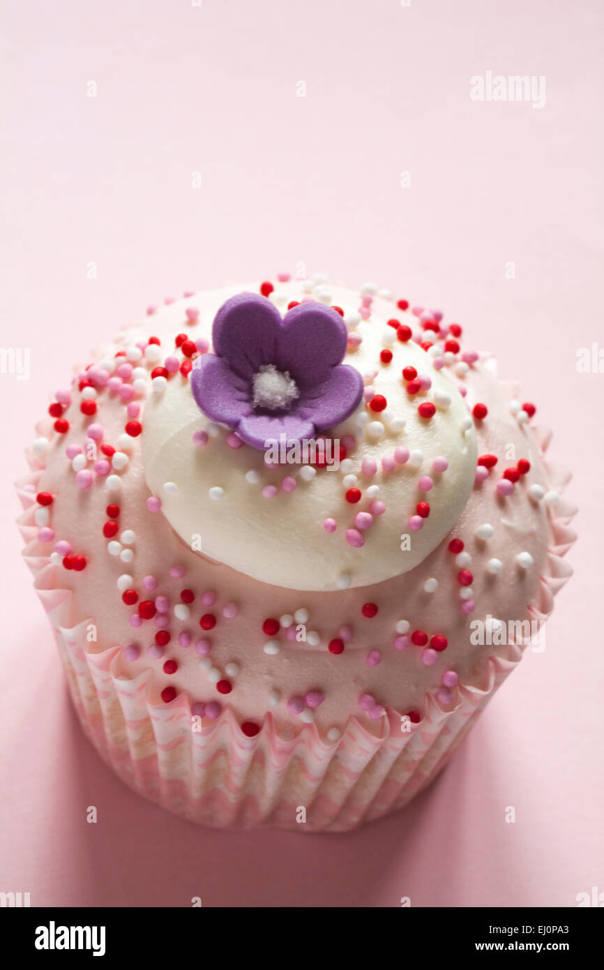 Tesco mit Liebe Erdbeeren und Sahne Cupcake mit Blume an der Spitze auf rosa Hintergrund isoliert Stockfoto