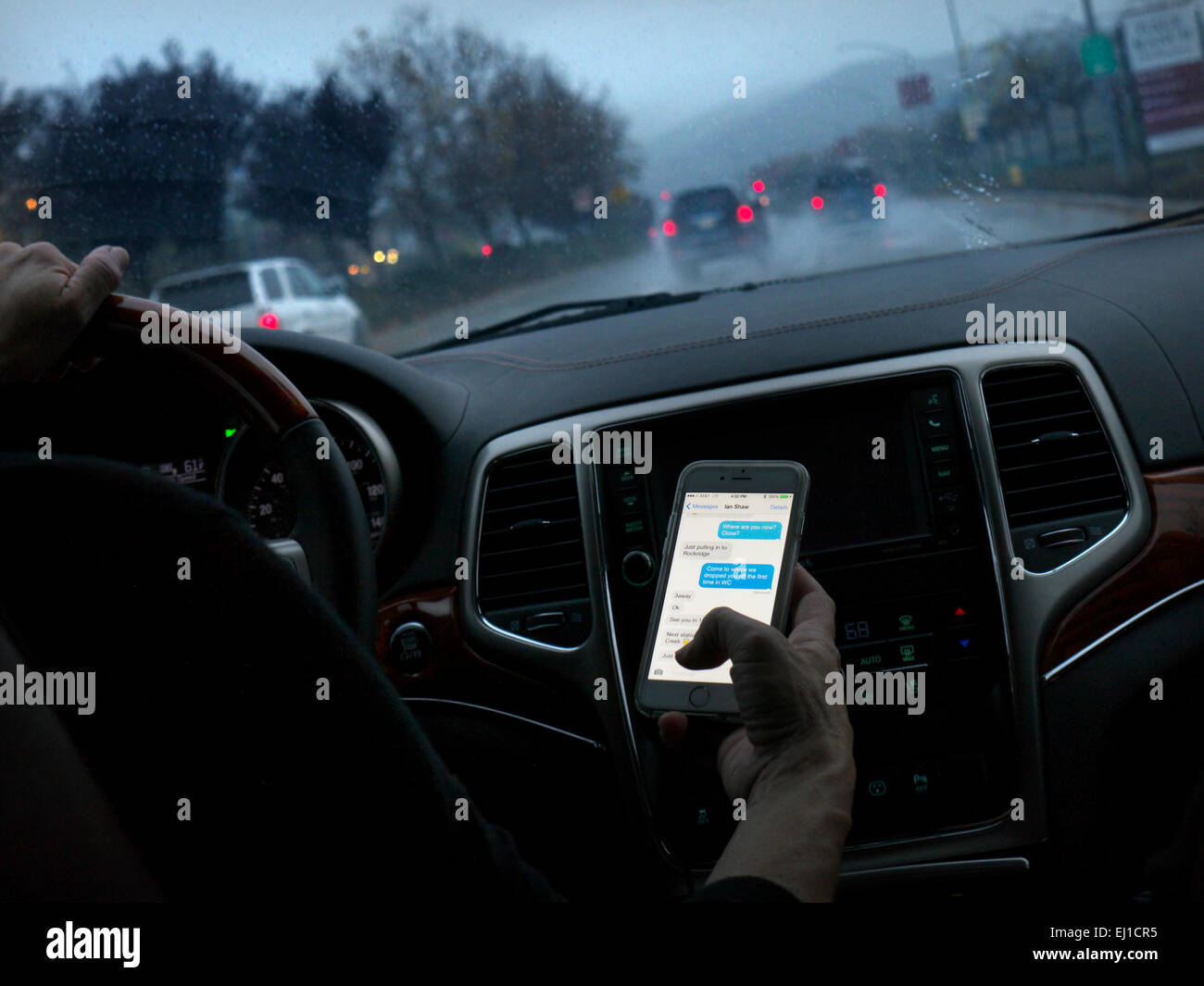 In dem Auto texting Fahrerin in l/h Fahrzeug fahren heimlich SMS-Smartphones während der Fahrt auf langen nassen Autobahn bei Dämmerung Stockfoto