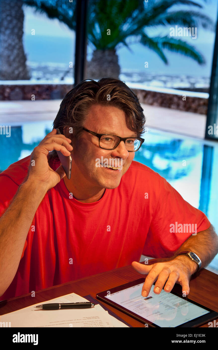 Glücklich reifer Mann mit seinem iPhone 6 Smartphone und iPad Luft Tablettcomputer in Luxus Urlaub Villa Hotel innen-Pool in der Dämmerung Stockfoto