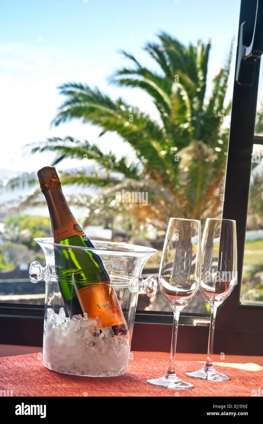 Champagner-Flasche & Gläser Zimmerservice auf Eis im Weinkühler am offenen Fenster der luxuriösen Urlaubsvilla/Hotelzimmer, Palmen & blauer Himmel dahinter Stockfoto