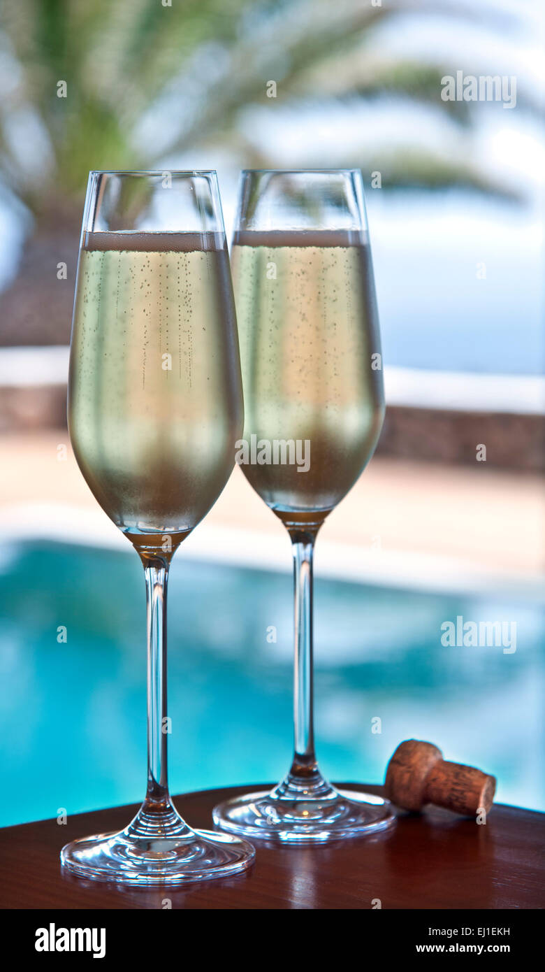 CHAMPAGNERURLAUB zwei frisch gegossene Gläser Champagner und Kork auf einem Terrassentisch im Freien mit luxuriösem Infinity-Pool und Palmen im Hintergrund Stockfoto