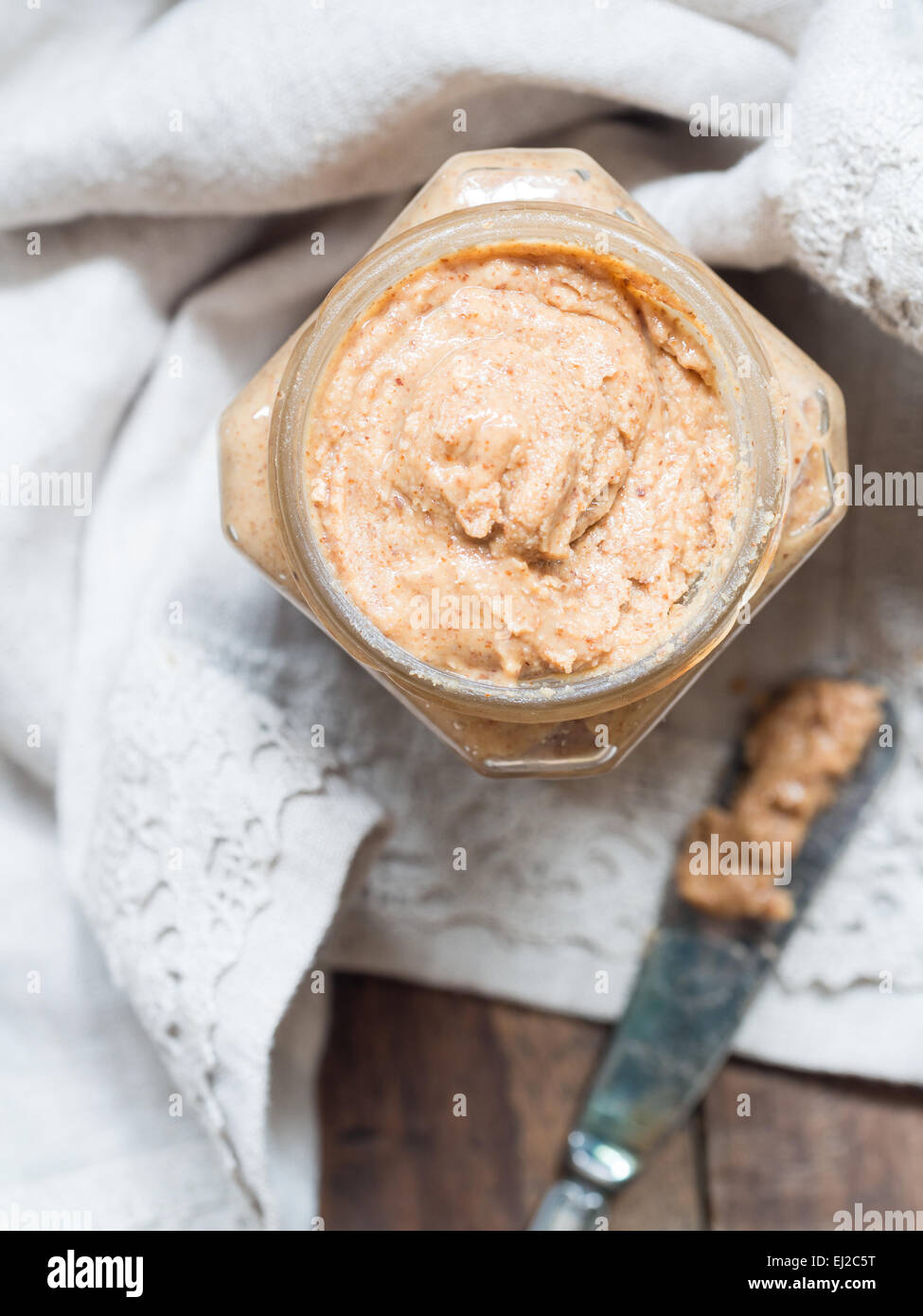 Vertikale Foto von hausgemachten natürliche Mandel-Butter in einem Glas auf rustikale Beige Tischdecke gelegt. Ansicht von oben. Stockfoto