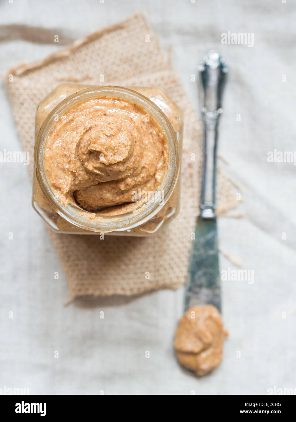 Vertikale Foto von hausgemachten natürliche Mandel-Butter in einem Glas auf rustikale Beige Tischdecke gelegt. Ansicht von oben. Stockfoto