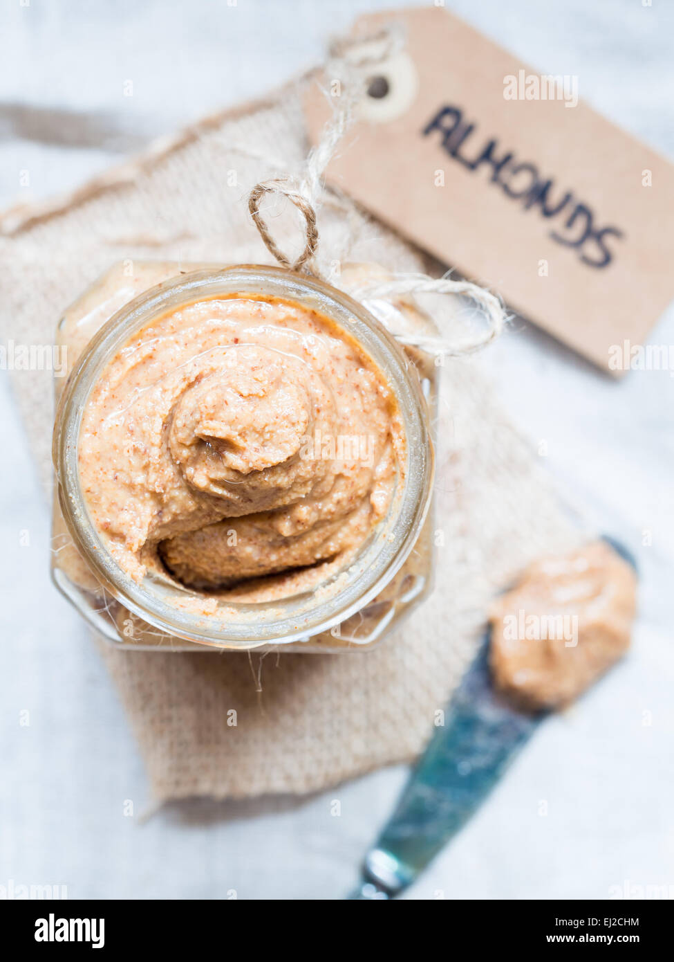 Vertikale Foto von hausgemachten natürliche Mandel-Butter in einem Glas auf rustikale Beige Tischdecke gelegt. Ansicht von oben. Stockfoto