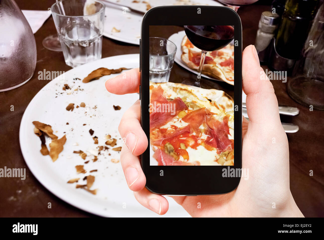 Fotografieren Food-Konzept - Tourist nimmt Bild der italienischen Pizza mit Parmaschinken und Glas Rotwein auf Smartphone, Italien Stockfoto