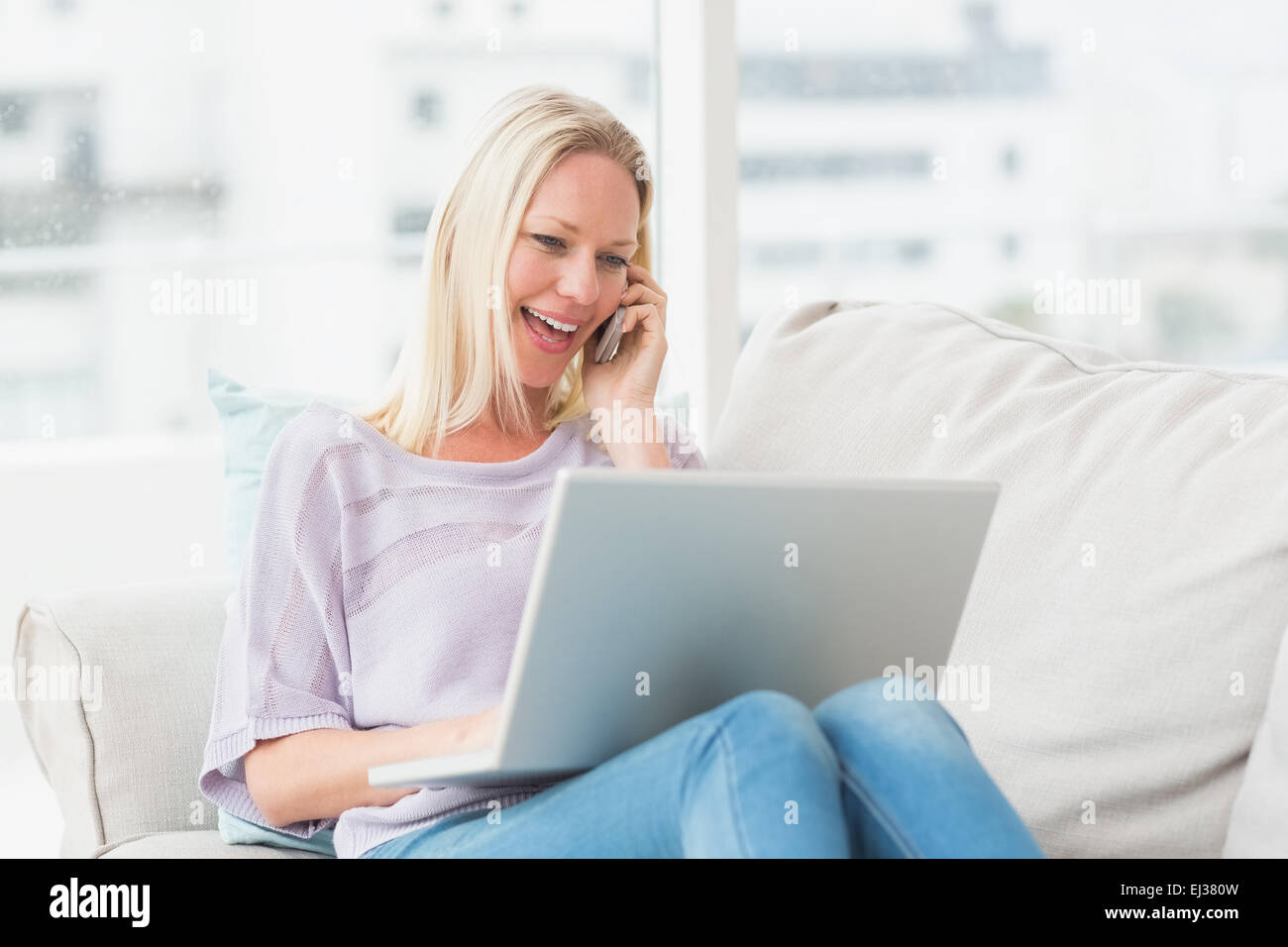 Frau am Telefon während mit Laptop auf sofa Stockfoto